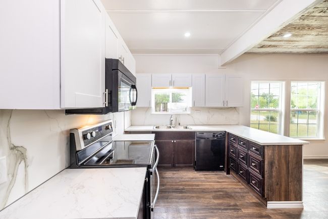 Kitchen featuring a peninsula, white cabinetry, black appliances, a sink, and decorative backsplash | Image 10