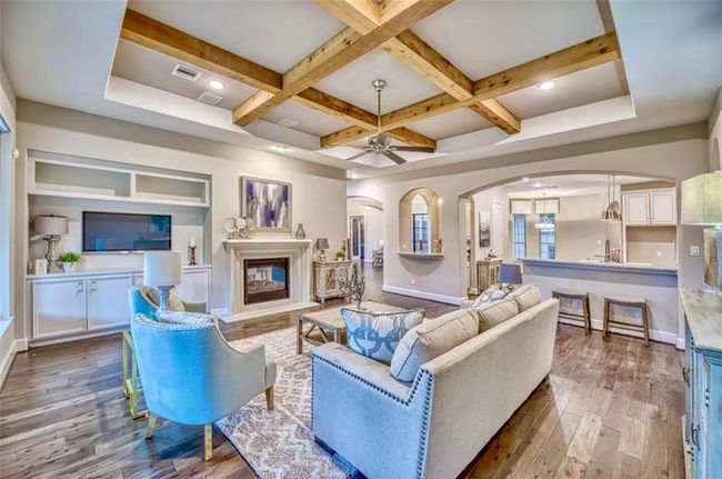 This spacious living room features elegant wood beam ceilings, a cozy fireplace, and hardwood floors. It seamlessly connects to an open kitchen area, creating a warm and inviting atmosphere perfect for entertaining. | Image 20