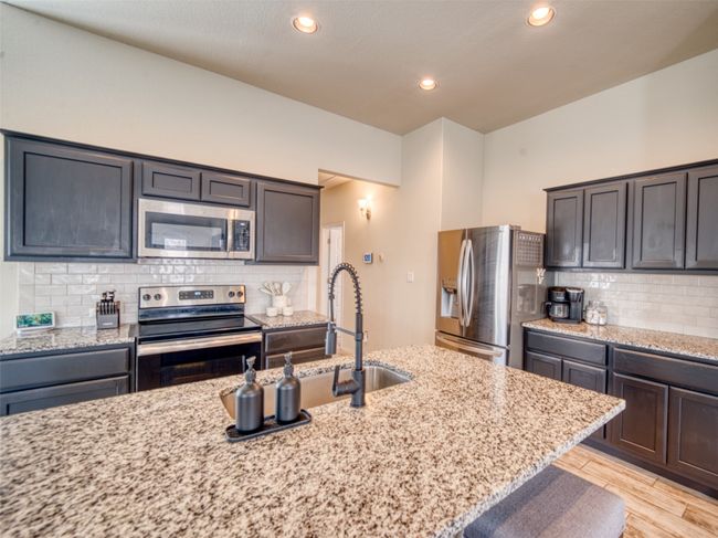 Kitchen featuring light stone countertops, backsplash, appliances with stainless steel finishes, and light wood-type flooring | Image 6