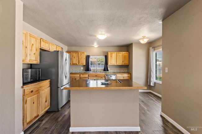 Kitchen with a textured ceiling, a kitchen island, dark wood finished floors, dark countertops, and stainless steel appliances | Image 12