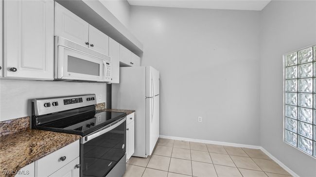 Kitchen with white cabinets, white appliances, baseboards, and dark stone countertops | Image 4