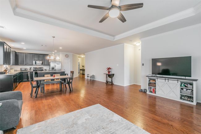 Living room featuring ceiling fan with notable chandelier, a tray ceiling, dark hardwood / wood-style flooring, and ornamental molding | Image 25