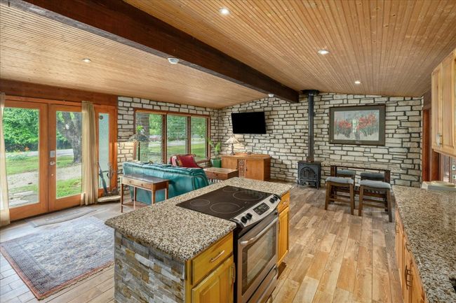 Kitchen with stainless steel electric stove, light wood finished floors, wooden ceiling, plenty of natural light, and a wood stove | Image 5
