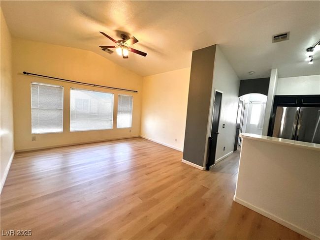 Unfurnished living room featuring visible vents, light wood finished floors, baseboards, a ceiling fan, and lofted ceiling | Image 11