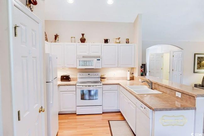 Kitchen featuring white appliances, a peninsula, white cabinets, light wood finished floors, and arched walkways | Image 15