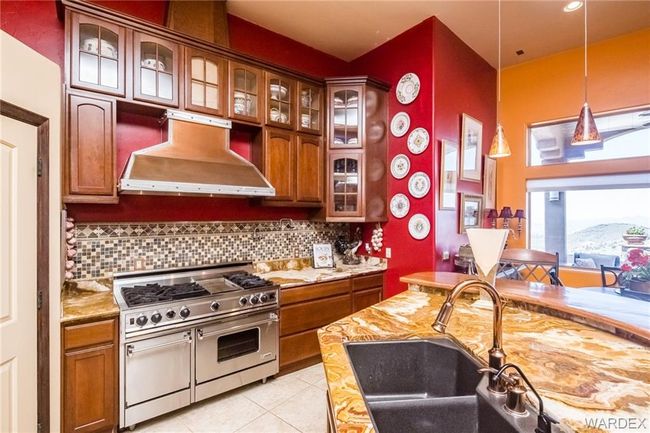 Kitchen featuring ventilation hood, range with two ovens, backsplash, light tile patterned floors, and brown cabinets | Image 38