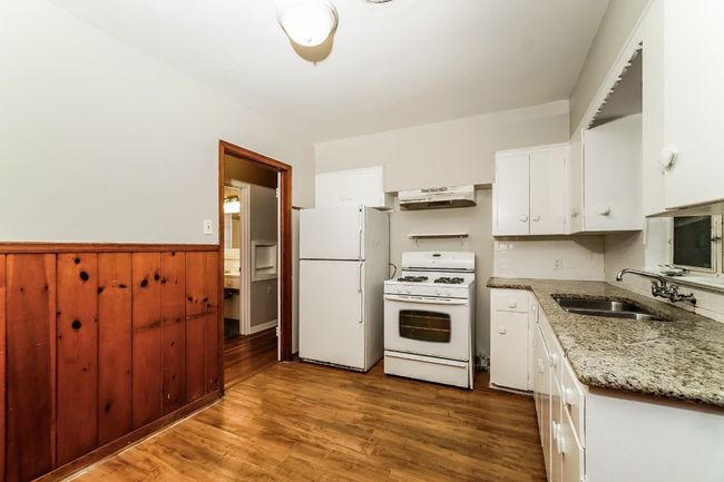 Kitchen with white appliances, under cabinet range hood, white cabinetry, wood finished floors, and wainscoting | Image 12