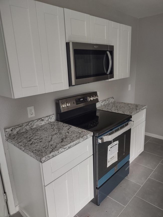 Kitchen with stainless steel appliances, white cabinets, light stone counters, and dark tile patterned floors | Image 7