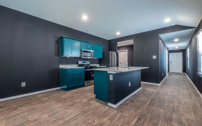 Kitchen featuring appliances with stainless steel finishes, dark wood-style flooring, an island with sink, blue cabinets, and lofted ceiling | Image 6