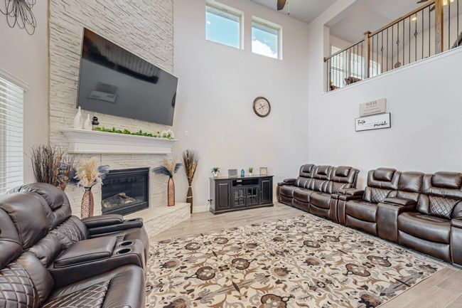 Living room featuring a fireplace, wood finished floors, a towering ceiling, and a ceiling fan | Image 5