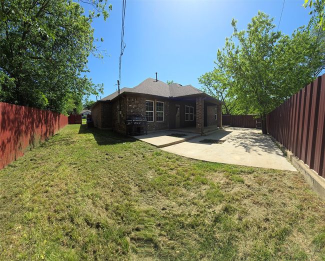 Rear view of house featuring brick siding, a patio area, a fenced backyard, and a lawn | Image 15