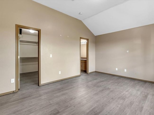 Unfurnished bedroom with baseboards, light wood-style flooring, a closet, a walk in closet, and lofted ceiling | Image 9
