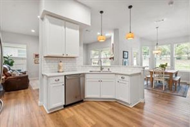 Kitchen featuring white cabinetry, light wood finished floors, a peninsula, light countertops, and stainless steel dishwasher | Image 13