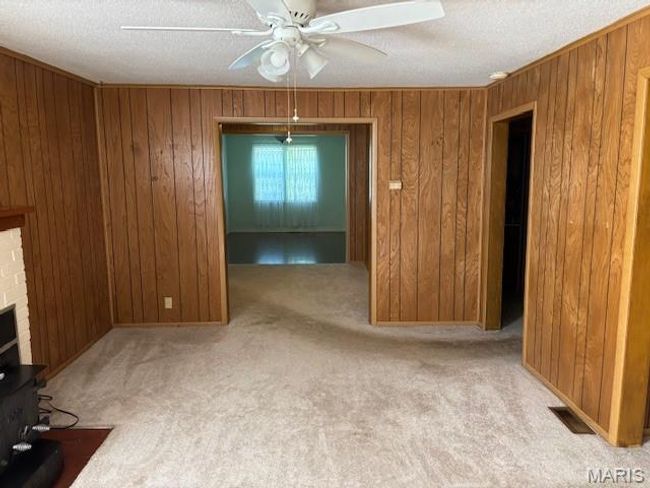 Unfurnished room featuring wood walls, a textured ceiling, carpet, a fireplace, and ceiling fan | Image 21