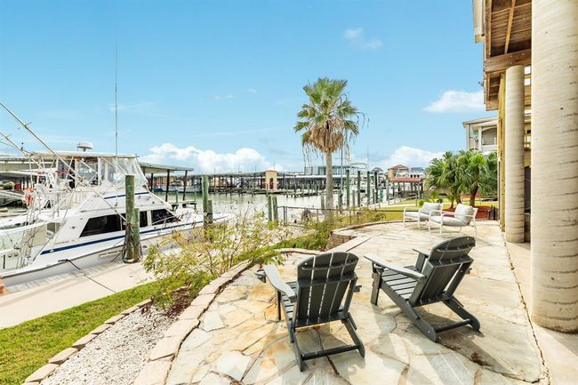 This waterfront property features a spacious stoned patio with comfortable seating, perfect for relaxing and enjoying views of the marina. The setting is enhanced by palm trees and easy dock access, ideal for boating enthusiasts. | Image 27
