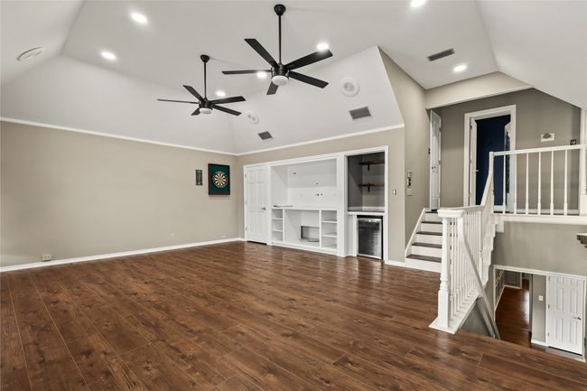 Unfurnished living room with vaulted ceiling, a ceiling fan, wood finished floors, beverage cooler, and recessed lighting | Image 9