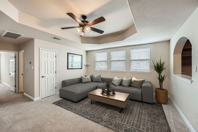 Carpeted living area with a raised ceiling, ceiling fan, baseboards, and visible vents | Image 10