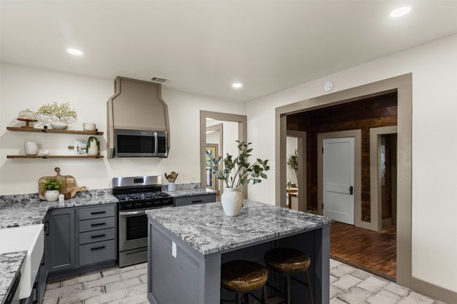 Kitchen with stainless steel appliances, gray cabinets, a breakfast bar, open shelves, and light stone countertops | Image 16
