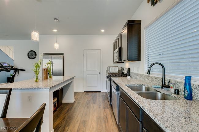 Kitchen with decorative light fixtures, stainless steel appliances, a sink, light stone countertops, and wood finished floors | Image 12