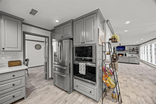 This photo showcases a modern open-concept kitchen and living area. The space flows seamlessly into a spacious living room with abundant natural light from large windows and a cozy fireplace, creating an inviting atmosphere. | Image 15