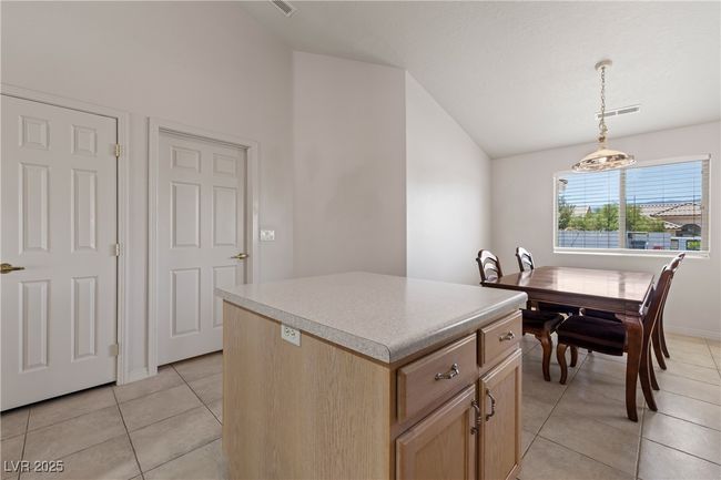 Kitchen with vaulted ceiling, a kitchen island, light tile patterned floors, light brown cabinets, and hanging light fixtures | Image 17