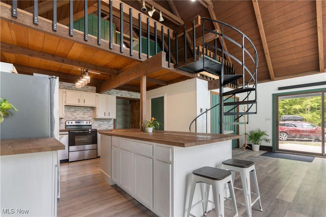 Kitchen with stainless steel appliances, butcher block counters, wood ceiling with exposed beams, light wood-style floors, and white cabinetry | Image 7