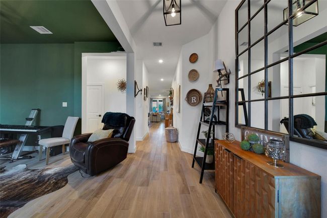 This photo showcases a modern, inviting hallway with wooden flooring, stylish decor, and a large mirrored wall. The space is bright, featuring a dark green accent wall and comfortable seating, creating a cozy and elegant atmosphere. | Image 11