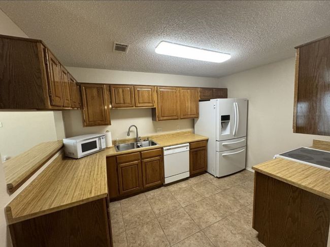 Kitchen featuring sink, white appliances, light tile flooring, and a textured ceiling | Image 9