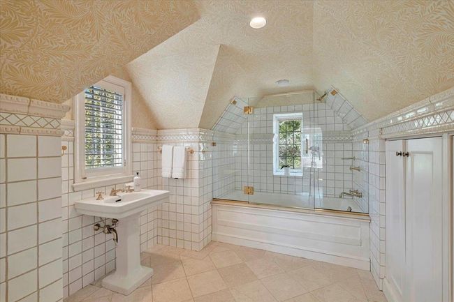 Timeless ensuite full bath with tile patterned floors, tile walls, combined bath / shower with glass door, and vaulted ceiling. | Image 19