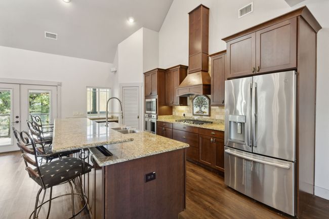 Kitchen with light stone counters, appliances with stainless steel finishes, high vaulted ceiling, an island with sink, and dark wood-type flooring | Image 8