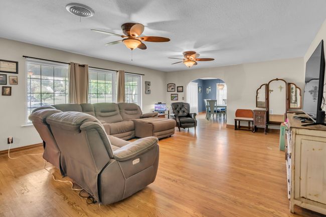 Living area with arched walkways, a ceiling fan, light wood finished floors, and a textured ceiling | Image 6
