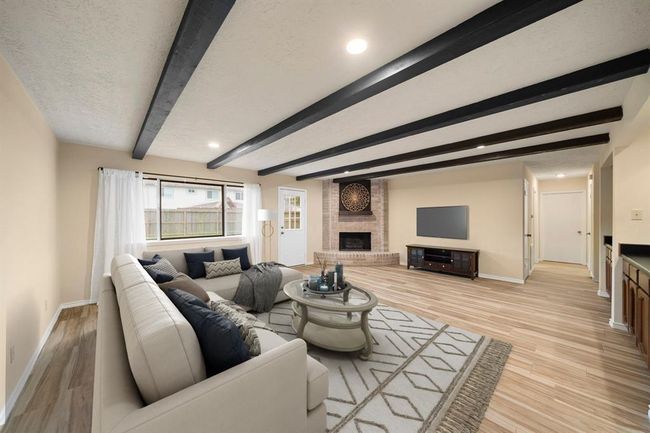Exposed ceiling beams and wide plank floors highlight the living area, which features a prominent brick fireplace as a focal point. This photo has been virtually staged. | Image 10