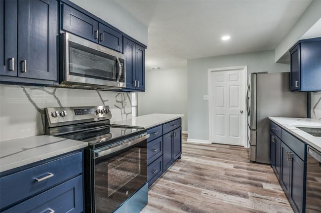 Kitchen with light wood-style floors, baseboards, recessed lighting, appliances with stainless steel finishes, and blue cabinetry | Image 12