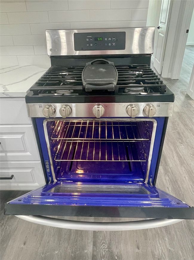 Kitchen view of stainless steel gas range, wood finished floors, and decorative backsplash | Image 6