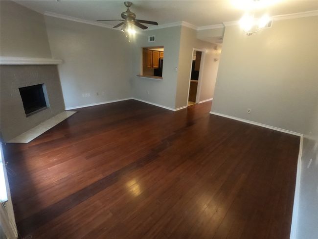 Unfurnished living room with a ceiling fan, dark wood-type flooring, a fireplace, baseboards, and ornamental molding | Image 6