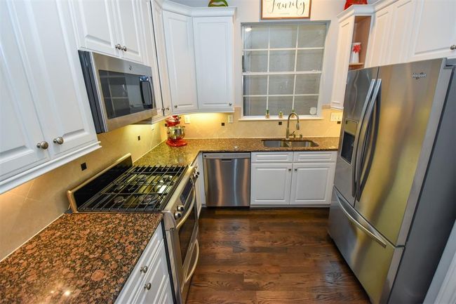 This is a modern kitchen featuring stainless steel appliances, white cabinetry, granite countertops, and hardwood flooring | Image 14