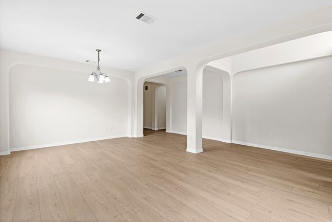 Unfurnished living room featuring a chandelier, arched walkways, and light wood finished floors | Image 6