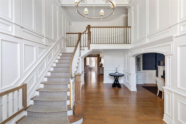 Stairs with a towering ceiling, a notable chandelier, wood finished floors, crown molding, and a decorative wall | Image 4