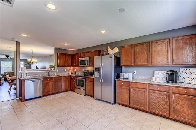 Kitchen featuring stainless steel appliances, brown cabinets, light stone counters, recessed lighting, and a chandelier | Image 8
