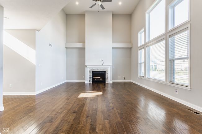 unfurnished living room featuring a ceiling fan, visible vents, and a high ceiling | Image 12