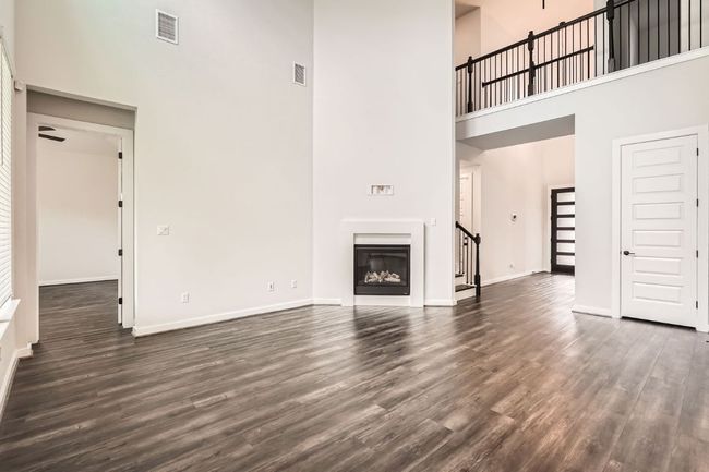 Unfurnished living room with a towering ceiling, dark wood-style floors, baseboards, and a glass covered fireplace | Image 5