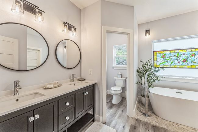 Bathroom with double vanity, a soaking tub, wood finished floors, toilet, and baseboards. | Image 16