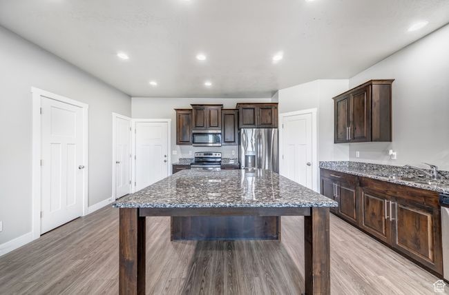 Kitchen featuring dark brown cabinetry, dark stone countertops, appliances with stainless steel finishes, and a sink | Image 6