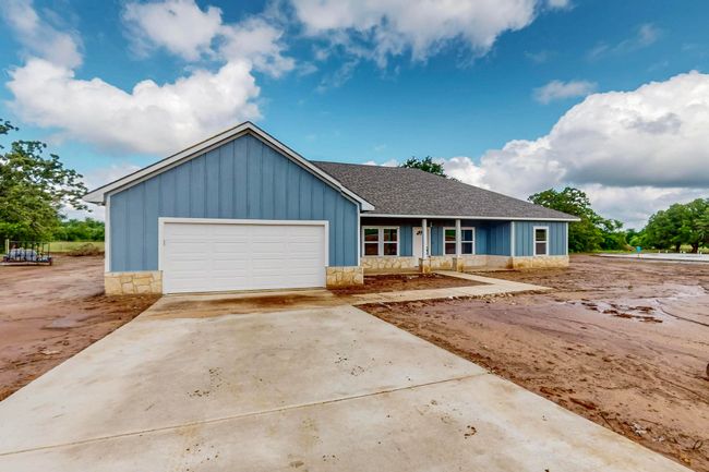 Ranch-style house with a shingled roof, concrete driveway, stone siding, board and batten siding, and an attached garage | Image 12