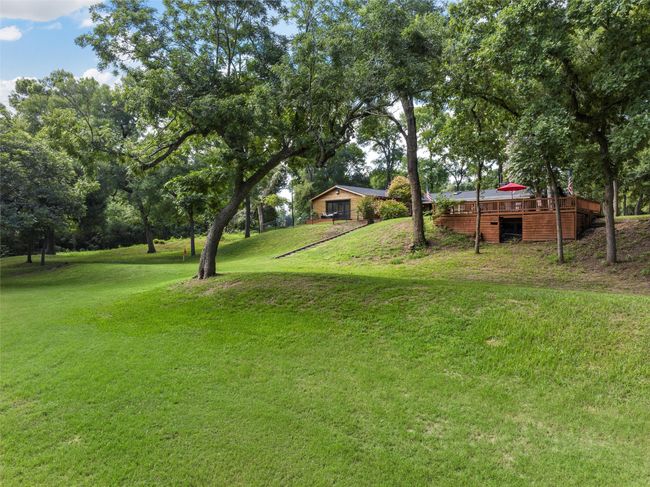 Wooden terrace with a fire pit, outdoor dining space, view of wooded area, and a yard | Image 27