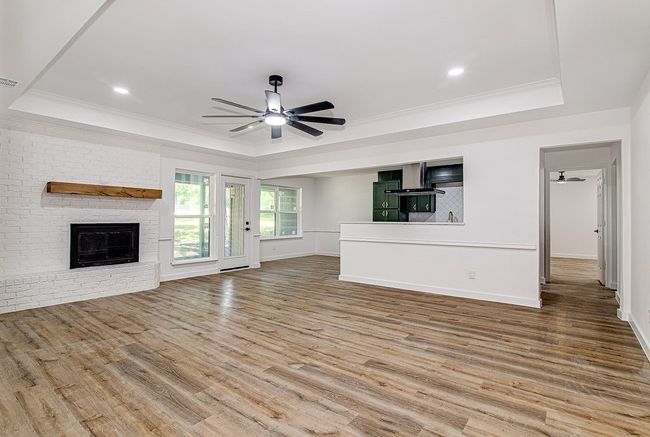 Unfurnished living room with a raised ceiling, a ceiling fan, wood finished floors, a brick fireplace, and ornamental molding | Image 9