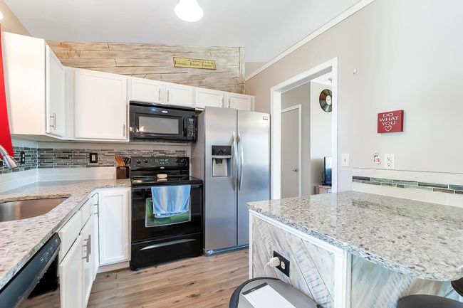 Kitchen with black appliances, white cabinets, backsplash, light stone countertops, and light wood-type flooring | Image 13