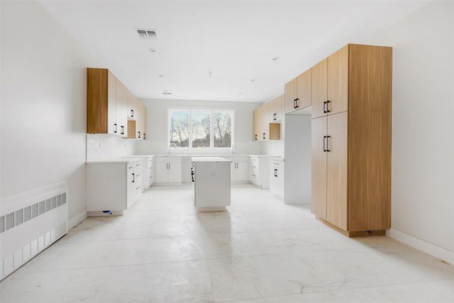 Kitchen with a center island, radiator heating unit, sink, and white cabinetry | Image 21