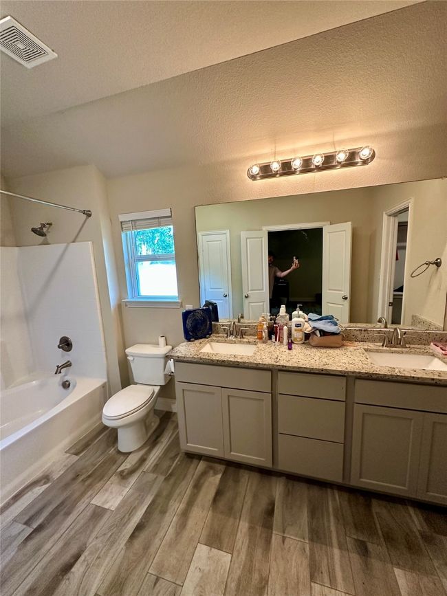 Bathroom with wood finished floors, shower / bath combination, double vanity, and a textured ceiling | Image 33