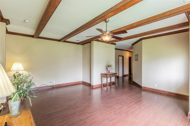 Unfurnished living room with ceiling fan, baseboards, wood finished floors, beamed ceiling, and ornamental molding | Image 10